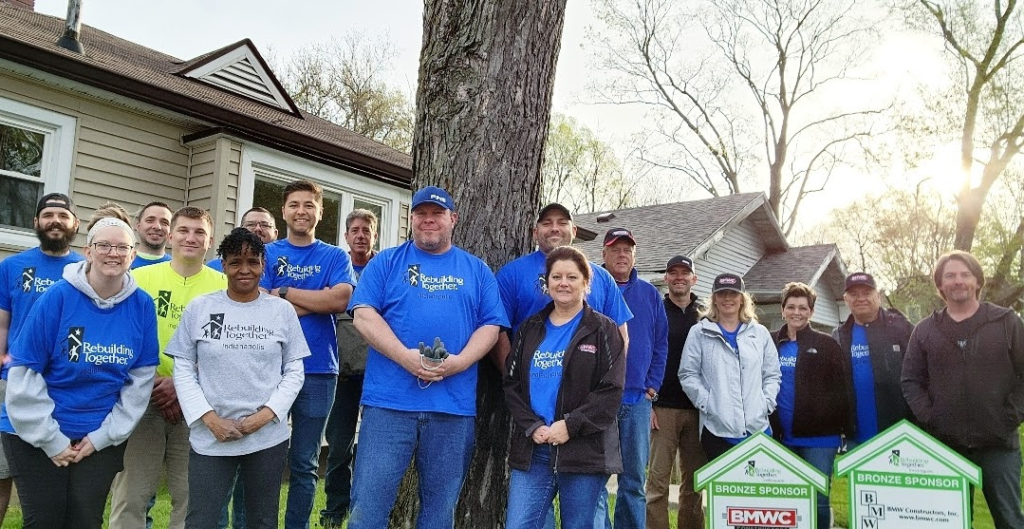 BMWC and Rebuilding Together Indianapolis members standing with blue shirts and signs in front of house