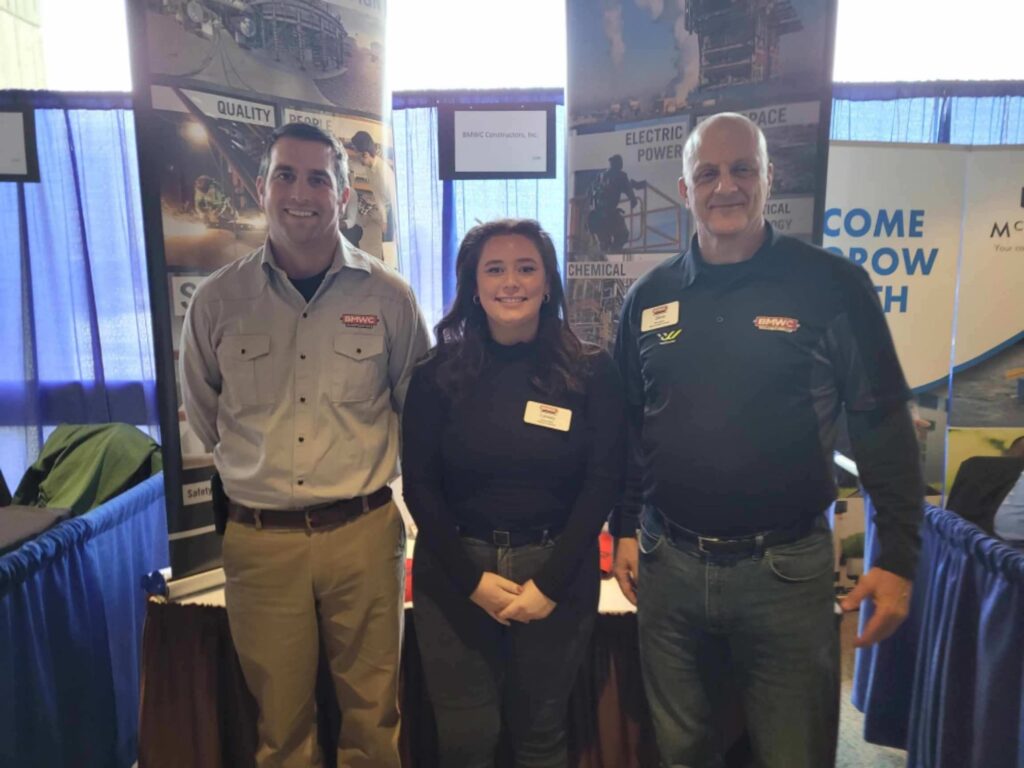 Three BMWC employees at career fair greeting potential interns. Two men with one woman in BMWC branded shirts