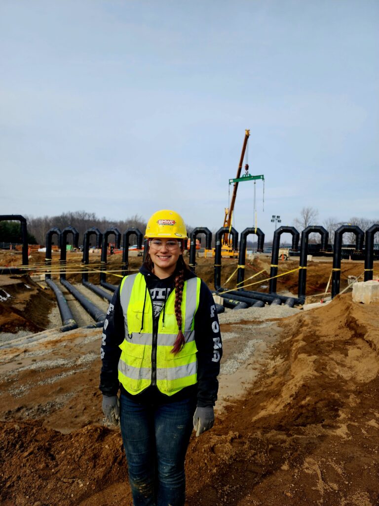 apprentice vanessa sheeler celebrating national women in construction week. posing on construcion site in front of candy cane piping system